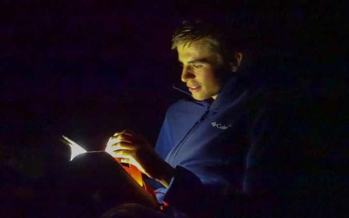 A person's face is illuminated by a flashlight as they read.